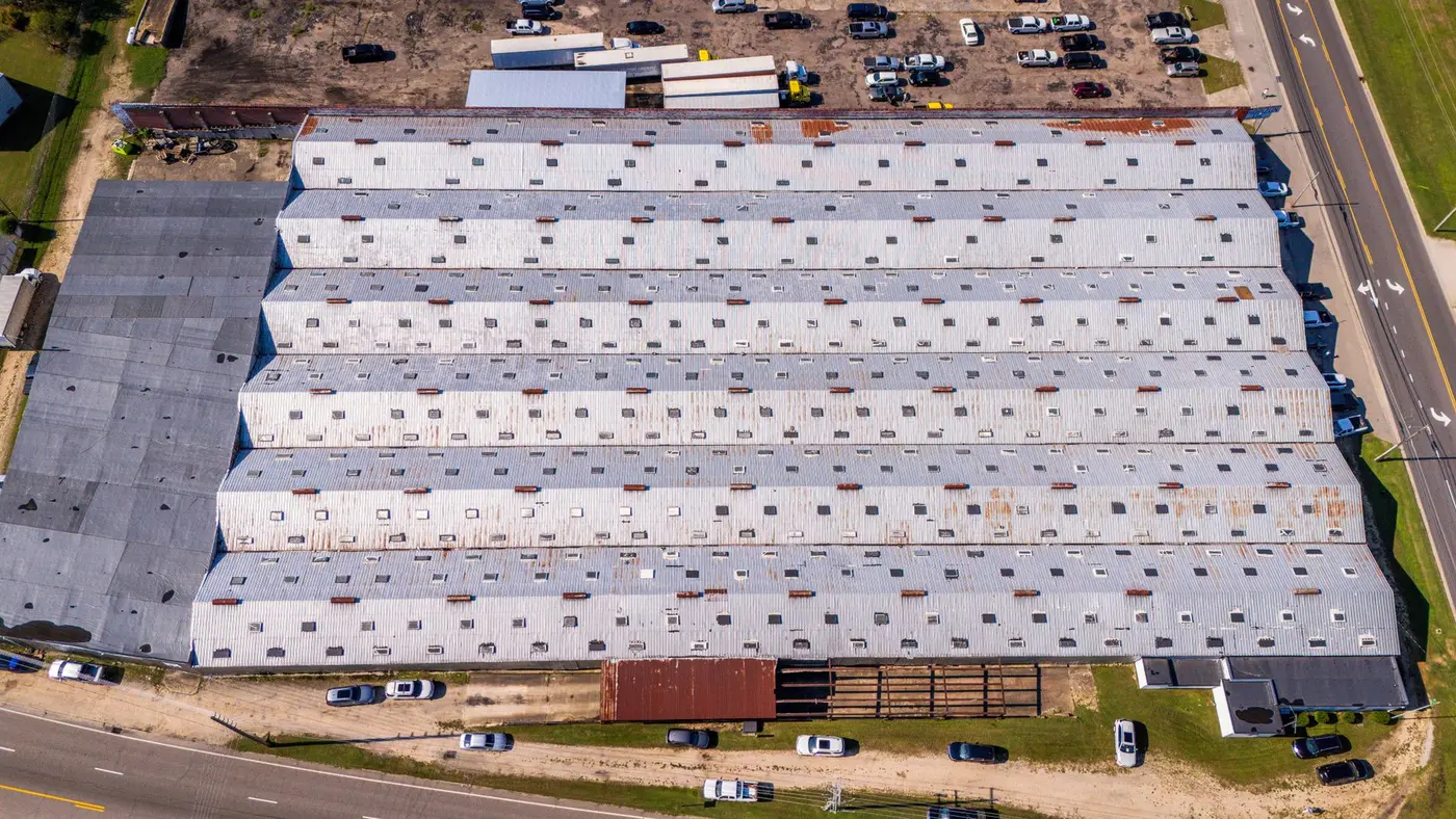 An overhead view of a large low-slope commercial roof covering a warehouse, with roof vents and curbs in regular rows