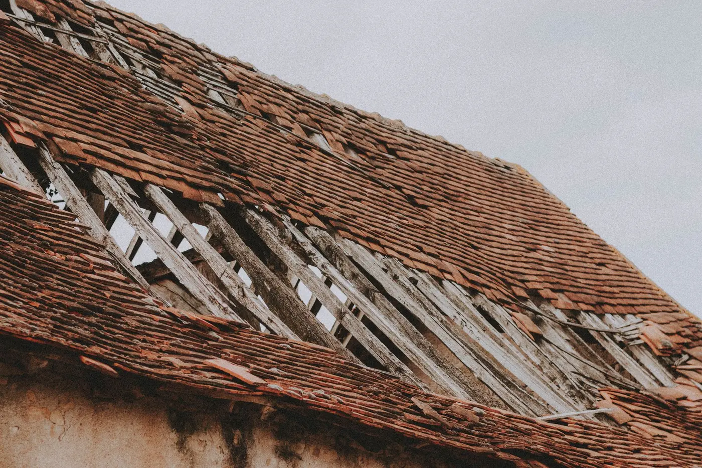 A failing tile roof with whole courses missing and the timber decking underneath exposed to the weather