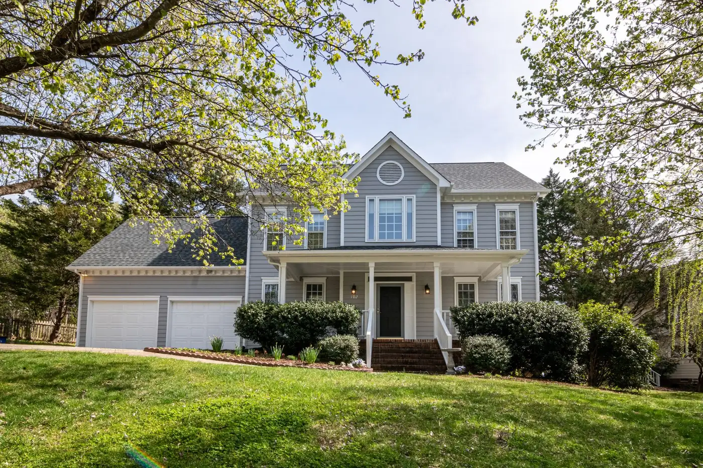 A grey two-storey suburban home with a shingle roof, set back on a lawn under mature trees